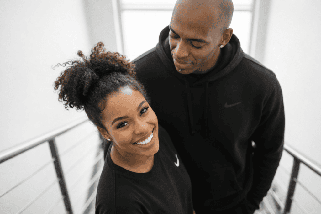 Sola and Peter standing together on a modern indoor staircase, dressed in black Nike outfits, with Sola looking up at the camera and Peter looking down toward her.