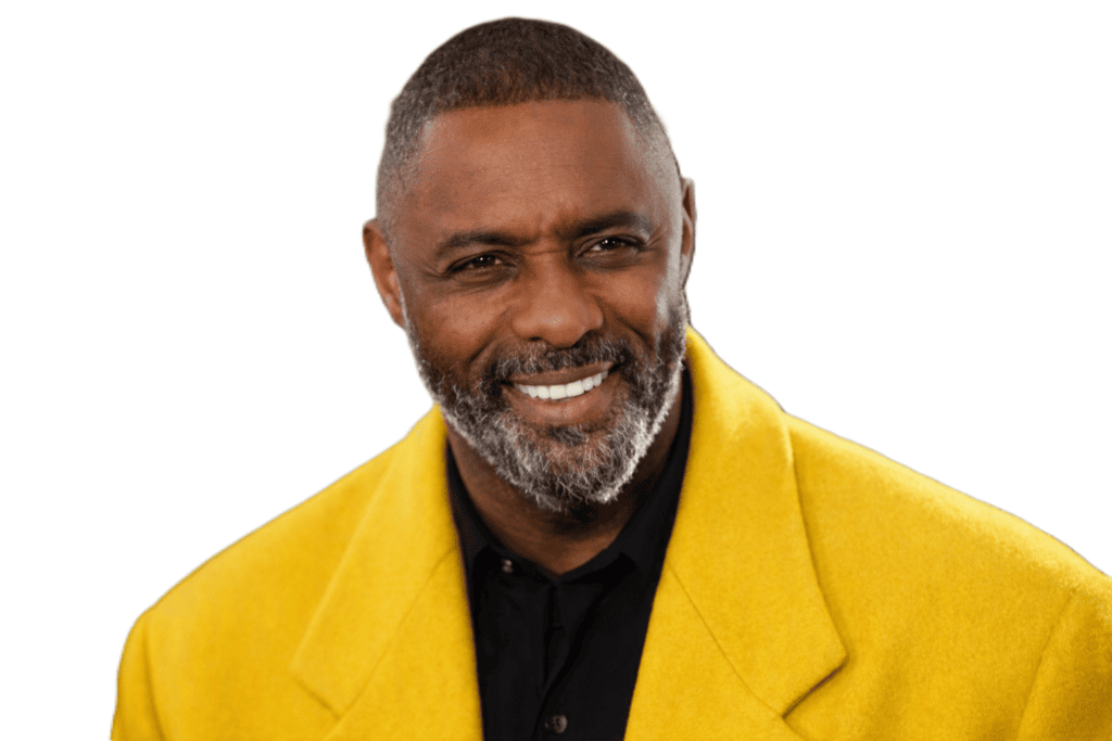 Idris Elba wearing a bright yellow overcoat and black shirt, smiling warmly against a blurred dark background.