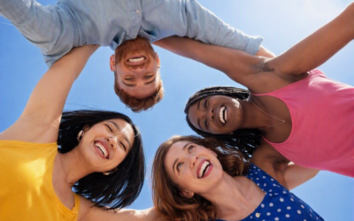 Four young adults smiling outdoors under a blue sky