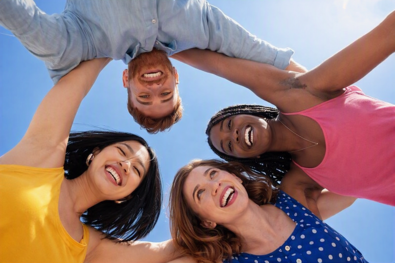 Four young adults smiling outdoors under a blue sky