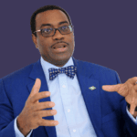 Akinwumi Adesina is wearing a blue suit and patterned bow tie, gesturing while speaking against a dark background.