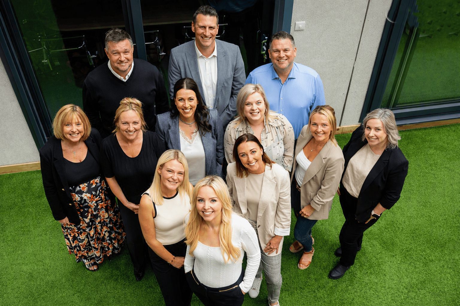A group of professionals standing on bright green artificial grass outside a modern building, symbolising Britain’s collaborative drive in artificial intelligence.
