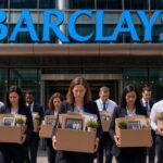 Diverse group of young male and female bank employees (white, Black and brown) carrying cardboard boxes of personal belongings as they exit a modern Barclays building after being laid of