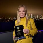 Jessica Stockmann holds the Golden Planet Award 2025 during an evening event overlooking the Frankfurt skyline, highlighting recognition for social engagement, sustainability and humanitarian commitment.