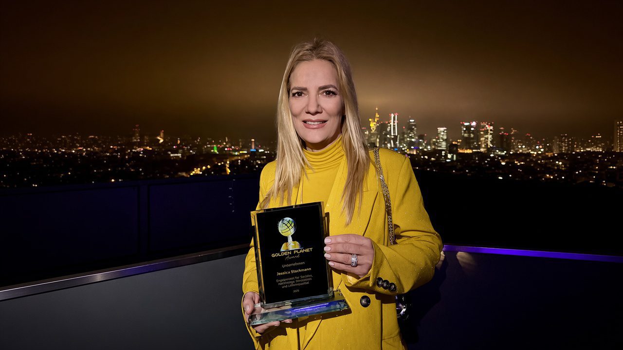 Jessica Stockmann holds the Golden Planet Award 2025 during an evening event overlooking the Frankfurt skyline, highlighting recognition for social engagement, sustainability and humanitarian commitment.